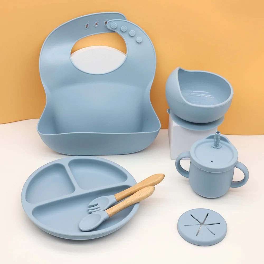 DearXime 7-piece dusty blue silicone baby mealtime set with suction plate, bowl, bib, cup, and wooden cutlery.