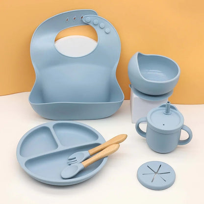 DearXime 7-piece dusty blue silicone baby mealtime set with suction plate, bowl, bib, cup, and wooden cutlery.